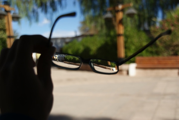 Hand holding eyeglasses against a blurred outdoor background.