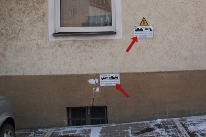 Two towing warning signs on an exterior wall, highlighted by red arrows.