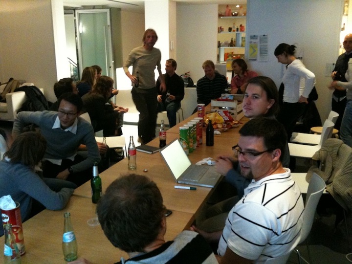 People gathered around a table with laptops, drinks, and snacks in a meeting room.