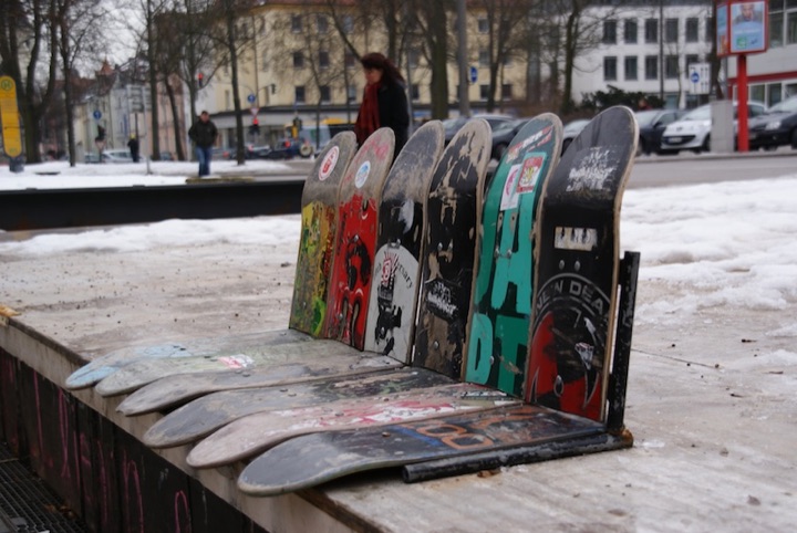 Several worn skateboard decks arranged on a snowy urban bench.