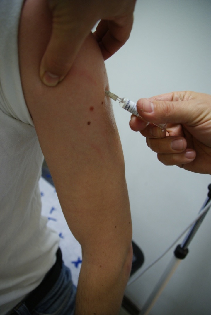 Close view of a syringe injecting an upper arm.