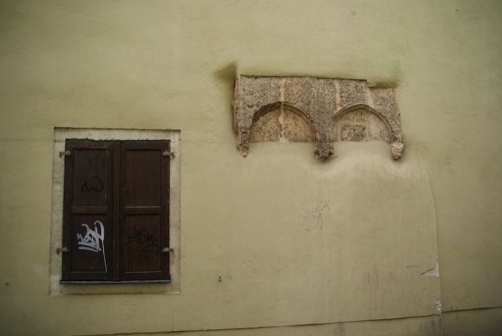 Old stone masonry fragment protruding from a pale plastered wall beside a window.