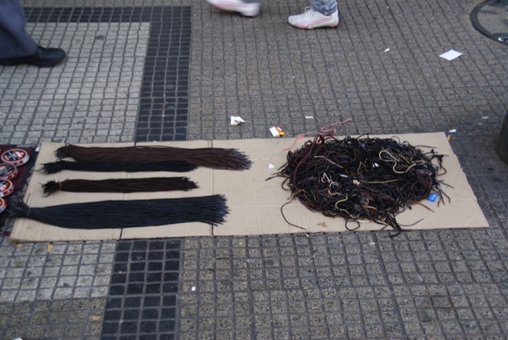 Bundles of shoelaces arranged on cardboard on a city pavement.