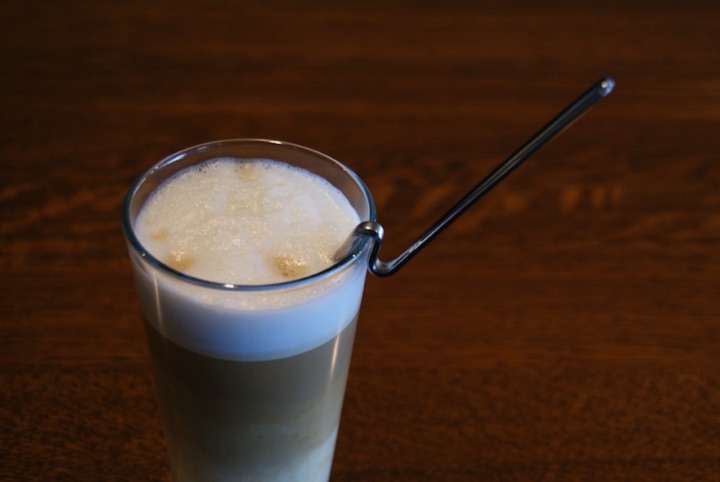 Tall glass of a foamy drink with a bent metal spoon hooked over the rim.
