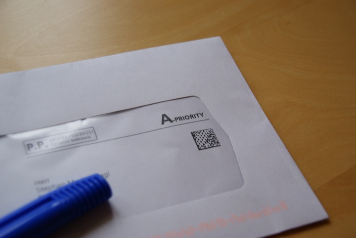 White A-Priority envelope and blue pen on a light tabletop.