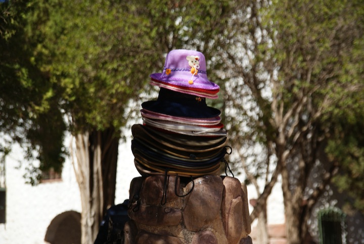 Stack of hats balanced on a pile of stones with trees behind it.