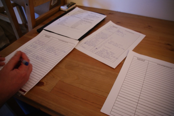 Hand writing on household-inventory forms spread across a wooden table.