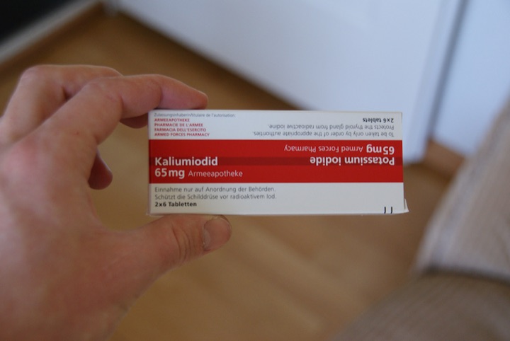 Hand holding a Swiss Armeeapotheke box of potassium iodide tablets.