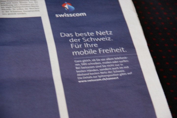 Close-up of a blue Swisscom newspaper advertisement reading “Das beste Netz der Schweiz. Für Ihre mobile Freiheit.”