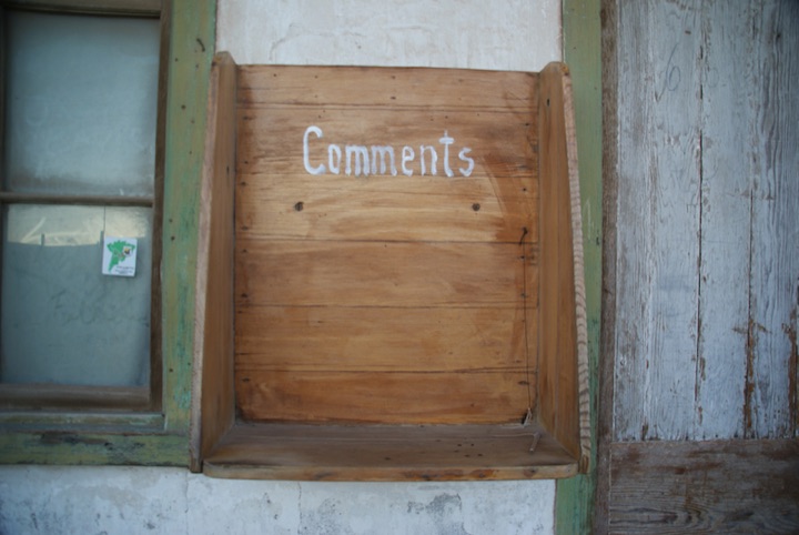 Wooden board labeled ‘Comments’ covering a wall opening beside a window.