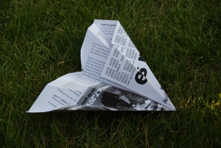 Folded paper airplane made from a printed page on grass.