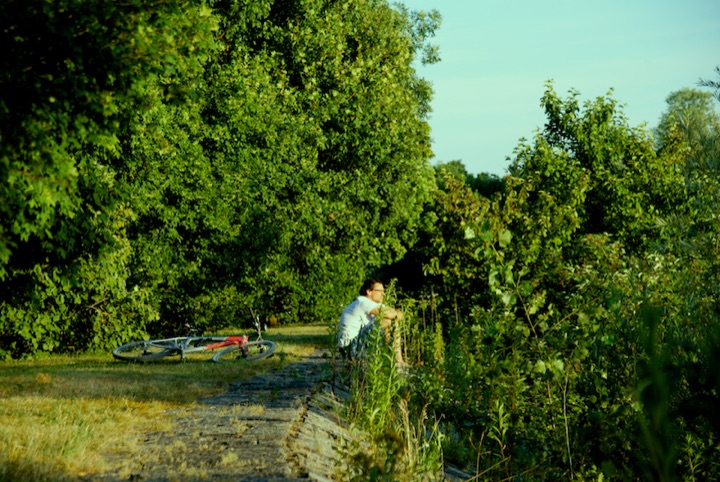 Person sitting beside a bicycle on a grassy path.