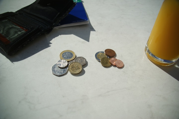 British, Swiss, and euro coins arranged on a table beside a wallet and orange juice.
