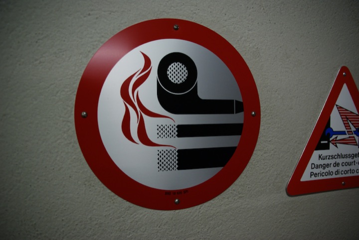 No-smoking sign beside a multilingual electrical hazard warning sign.