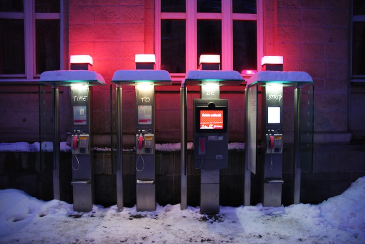 Four public telephone kiosks standing in snow beneath a red-lit building.