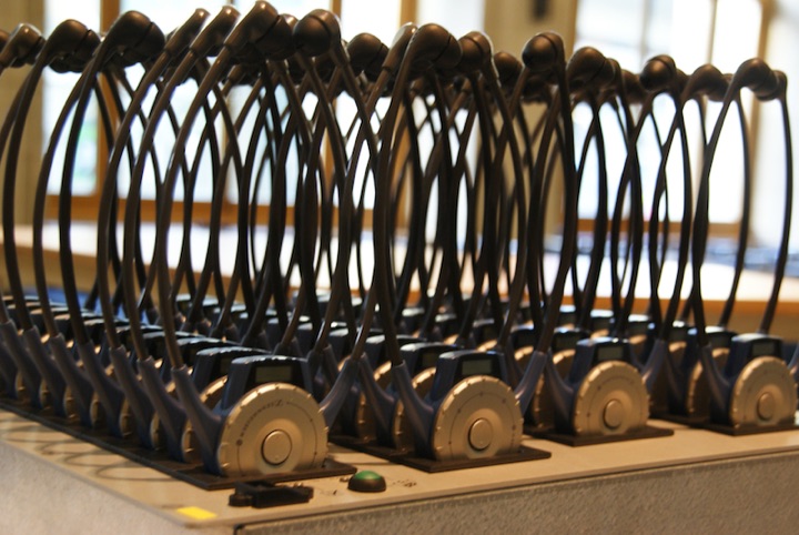 Rows of tour-guide earpiece devices in charging stands.