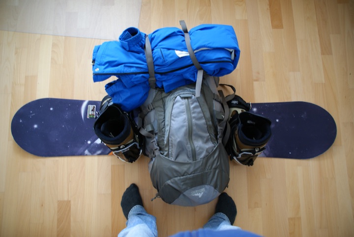 One snowboard with a backpack, boots, and a blue jacket on top, viewed from above.