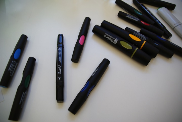 Black permanent markers with colored caps scattered on a white surface.