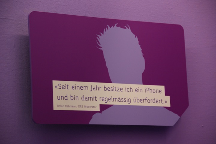 Purple museum exhibition panel with a white silhouette and a German-language quote attributed to Robin Rehmann about feeling overwhelmed by an iPhone.