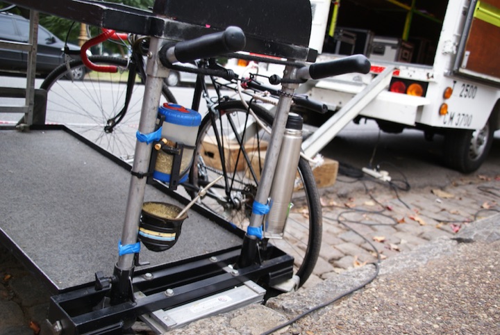 A bicycle-mounted metal frame holding a thermos and containers.