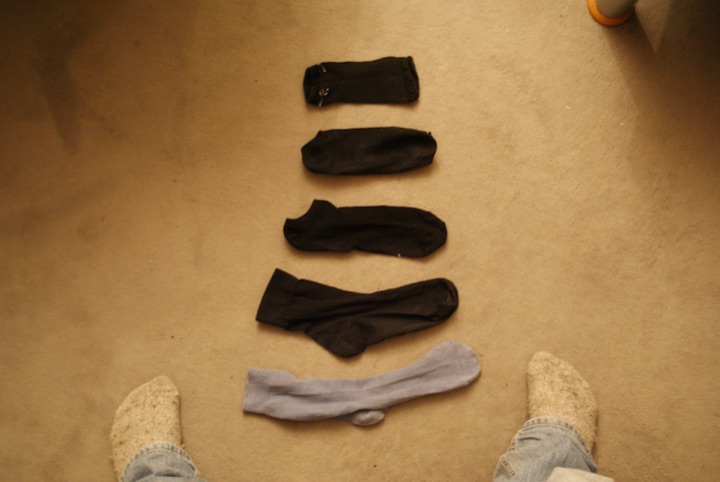 Five socks arranged on a beige carpet between a person’s feet.
