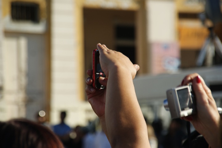 Hand holding a mobile phone beside another hand holding a compact pocket camera.
