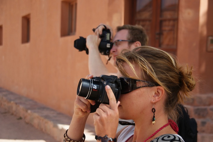 Two people holding DSLR cameras against a salmon-colored wall.