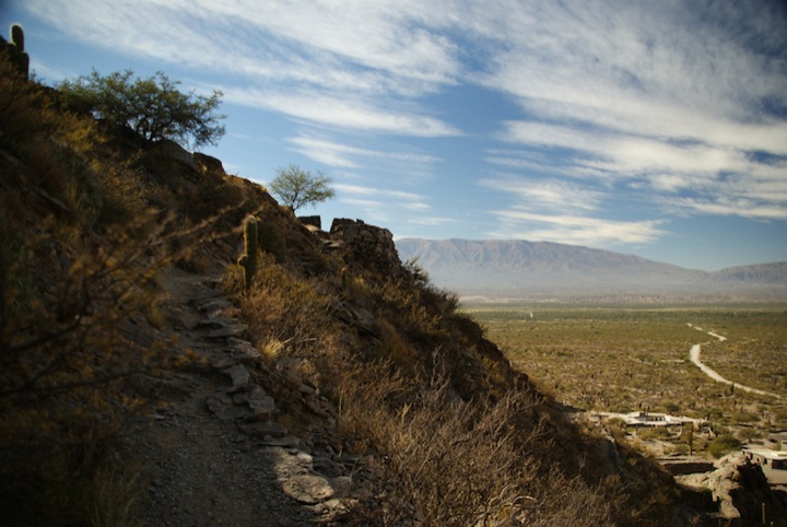 Rocky hillside overlooking a broad valley and distant mountains under a cloudy sky.