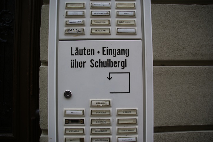 Apartment-building intercom with nameplates and a German direction sign.