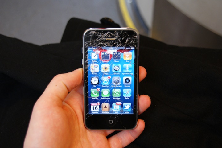 Hand holding a smartphone with a cracked screen.