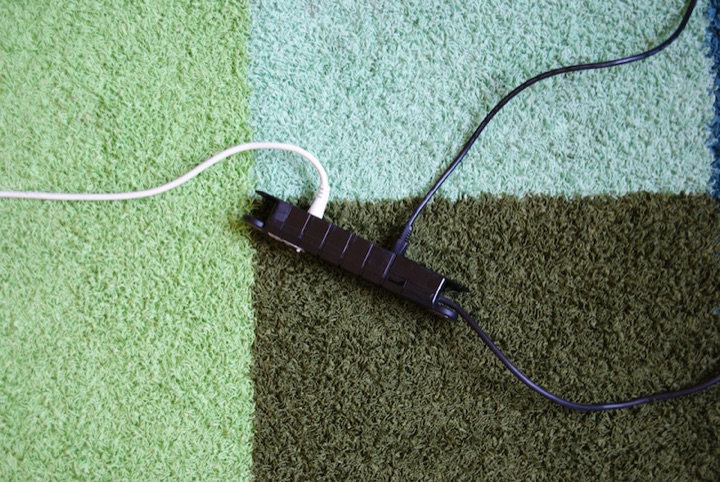 Black power strip with white and black cables on a patterned rug.