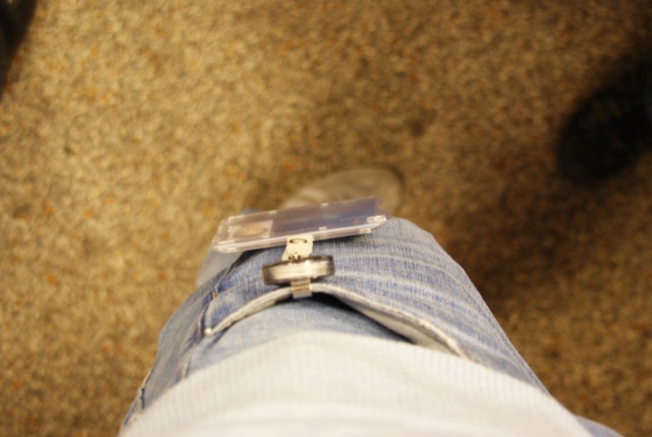 A clear plastic identity badge clipped to the waistband of blue jeans.