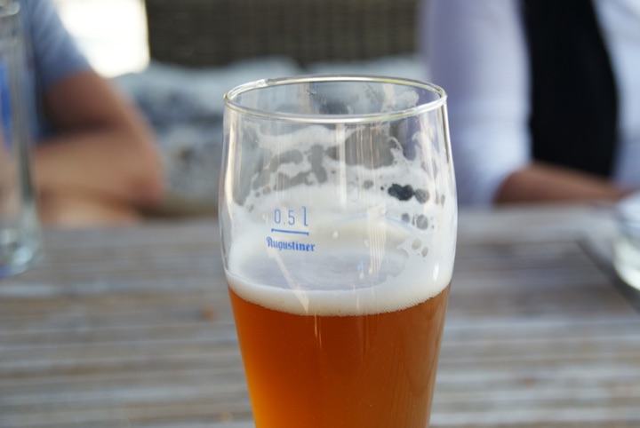 Partly filled beer glass on a wooden table with people in the background.