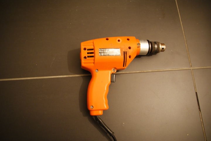 Orange electric drill lying on a tiled floor.