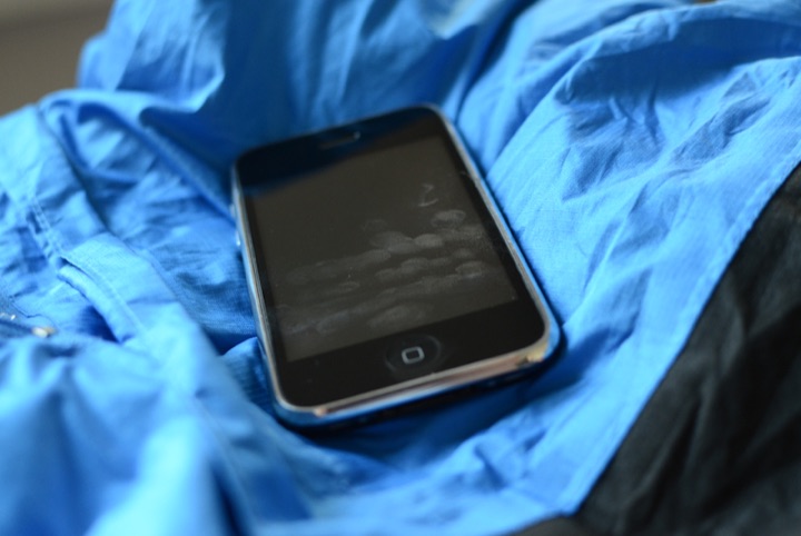 Black smartphone with fingerprint marks on its screen lying on a blue jacket.