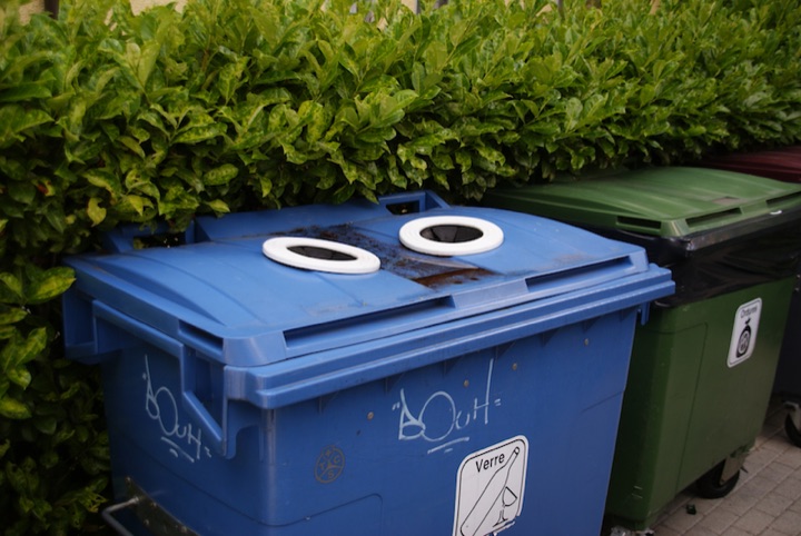 Blue recycling bin with two white-rimmed circular openings on its lid beside a green bin.