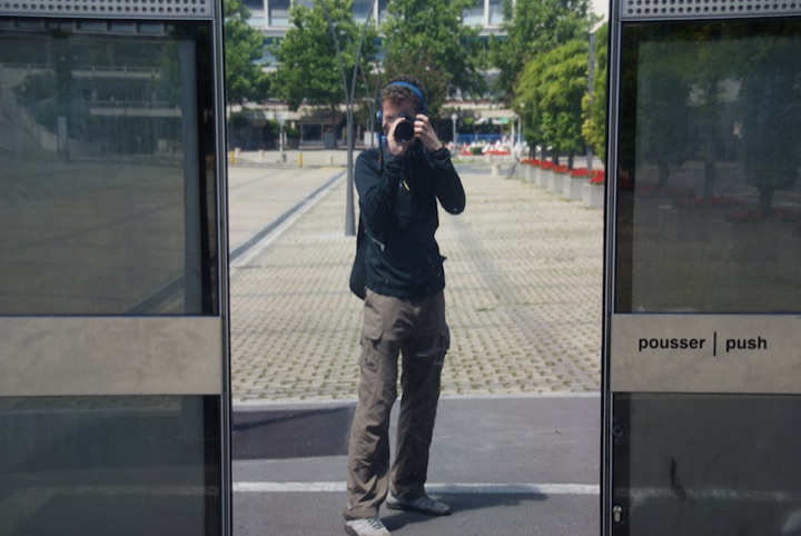 Person holding a camera reflected in a glass door beside a bilingual ‘push’ sign.