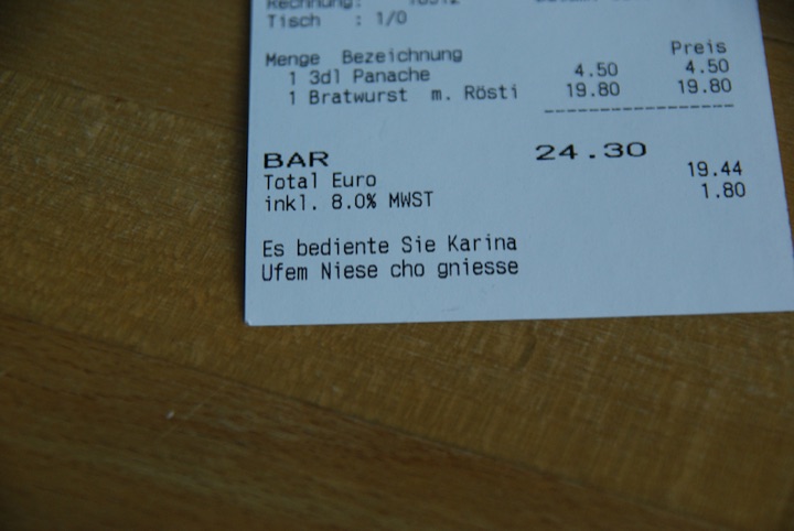 Restaurant receipt on a wooden table showing an itemized bill and a personalized service message.
