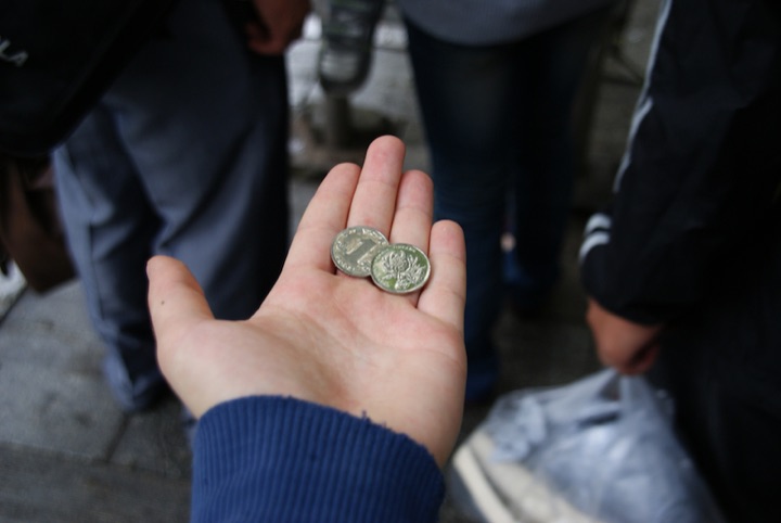 Open hand holding two Chinese coins among people standing on a pavement.