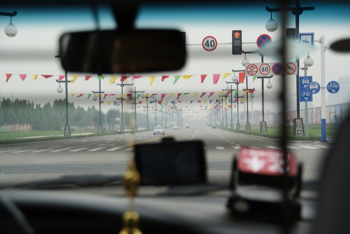 View through a vehicle windshield down a broad road lined with traffic signs and colorful flags.