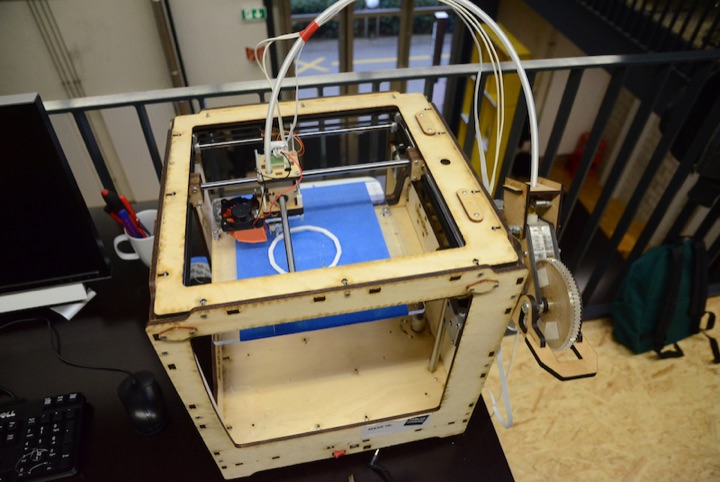 Wooden desktop 3D printer with exposed wiring and filament tubing.