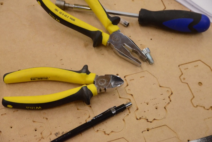 Yellow-handled pliers and laser-cut wooden pieces on a workbench.