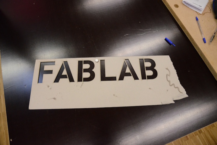 Laser-cut sign reading ‘FABLAB’ on a worktable.