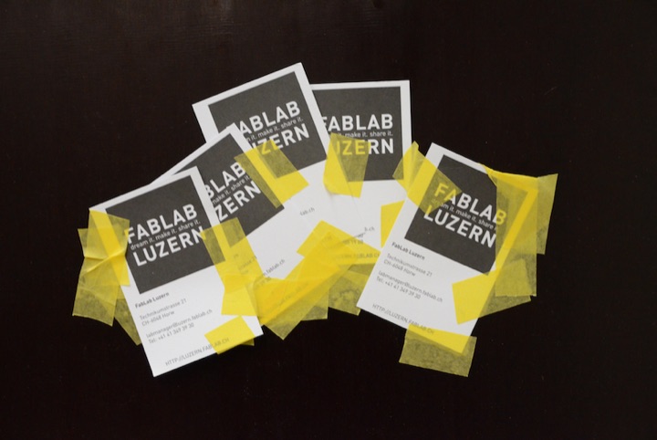 FabLab Luzern cards held down with yellow tape on a black table.