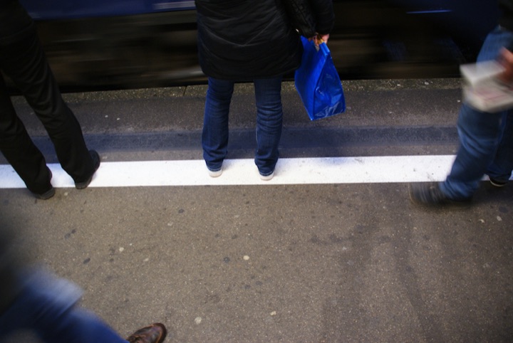 People standing beside a train at a platform edge; one person holds a bright blue bag.