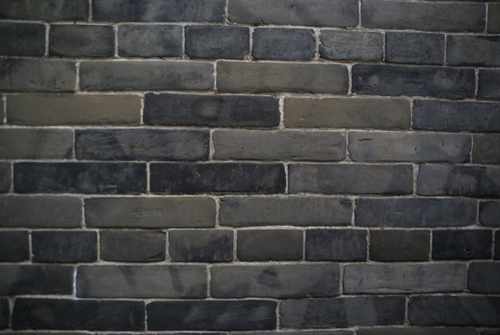 Close view of a dark gray brick wall with irregularly colored bricks.