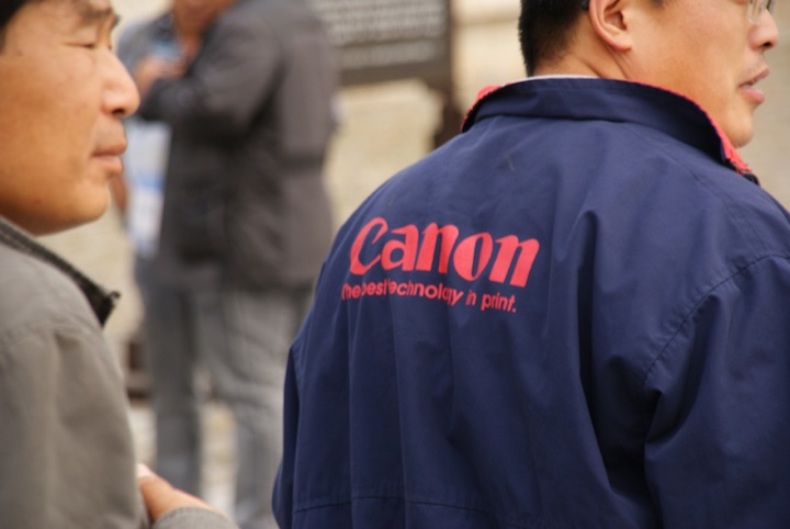 Man in a blue Canon-branded jacket seen from behind.