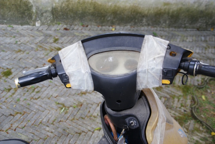 Top view of a scooter handlebar and dashboard wrapped in white duct tape.
