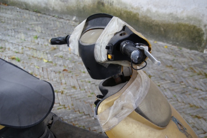 Close view of a scooter handlebar and headlight wrapped in white duct tape.