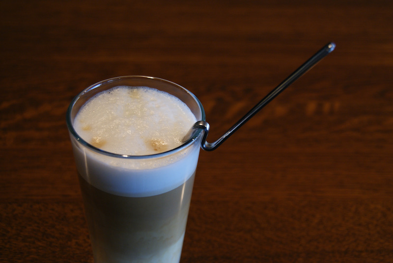 Tall glass of a foamy drink with a bent metal spoon hooked over the rim.